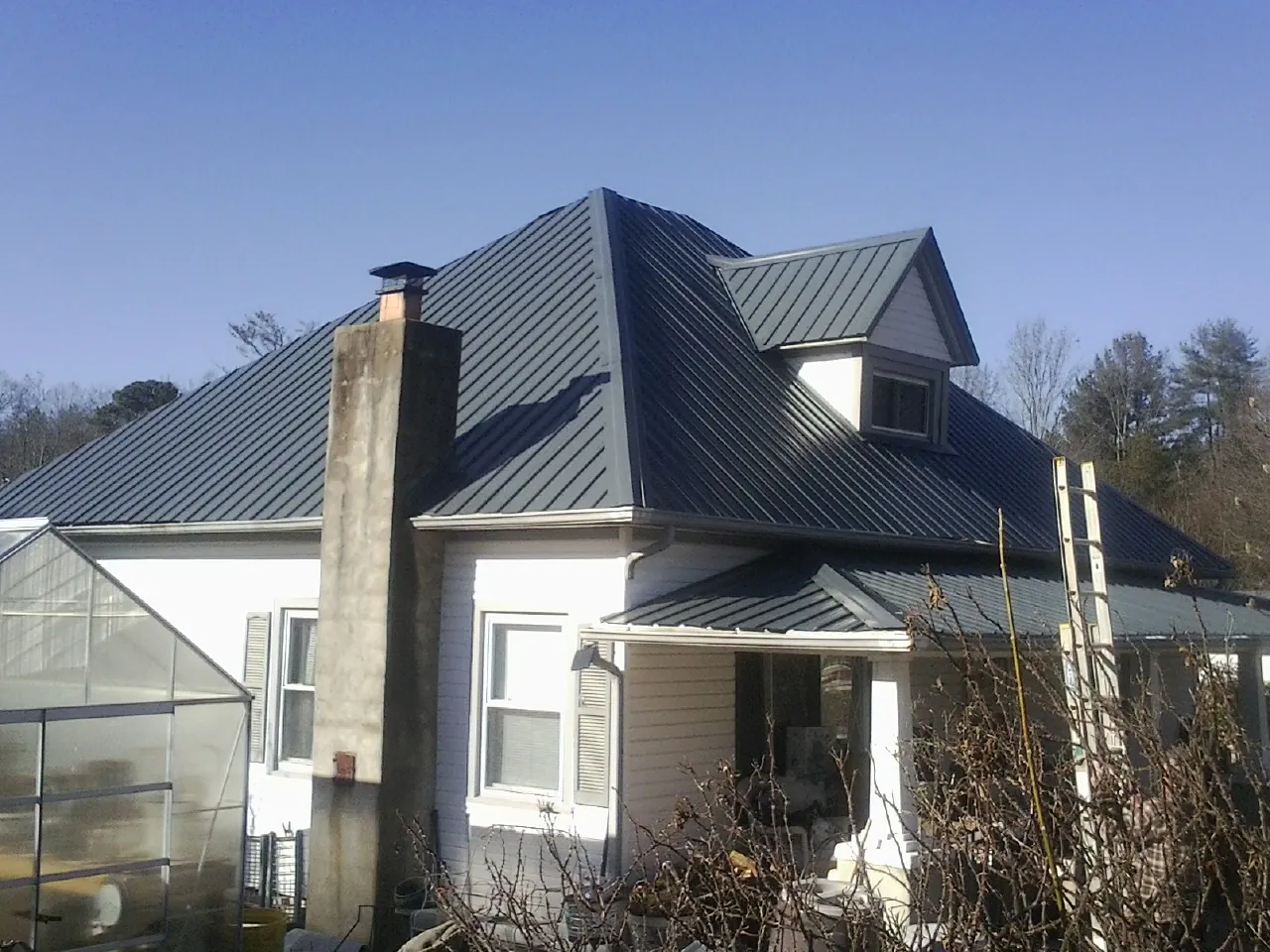 Dark blue standing seam metal roof on a white farmhouse with dormer — Slate & Tile Roof Repair by Roofing Brothers in Shattuck