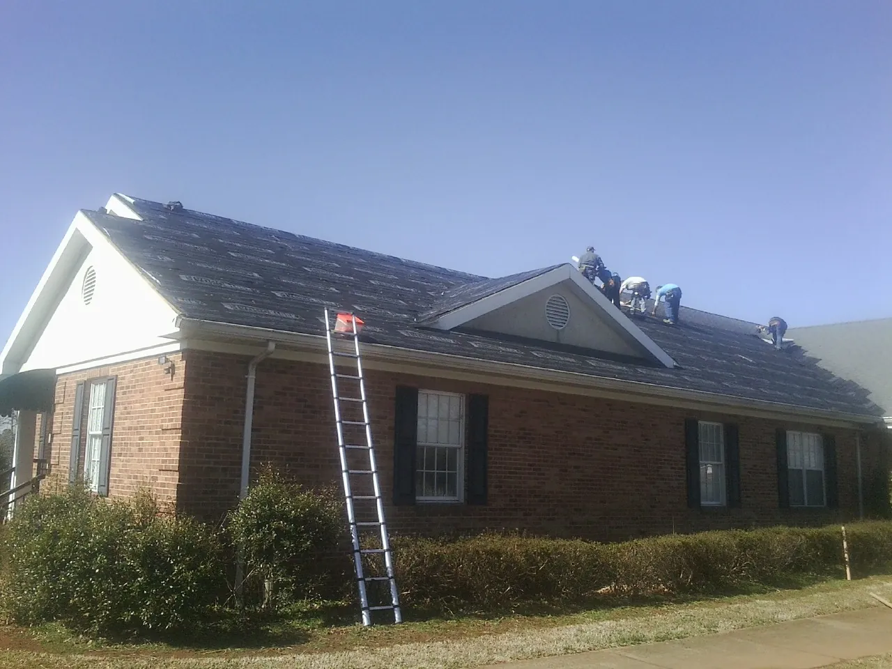 Crew tearing shingles off a brick ranch roof with a ladder set — Emergency Roof Repair work by our crew in Shattuck