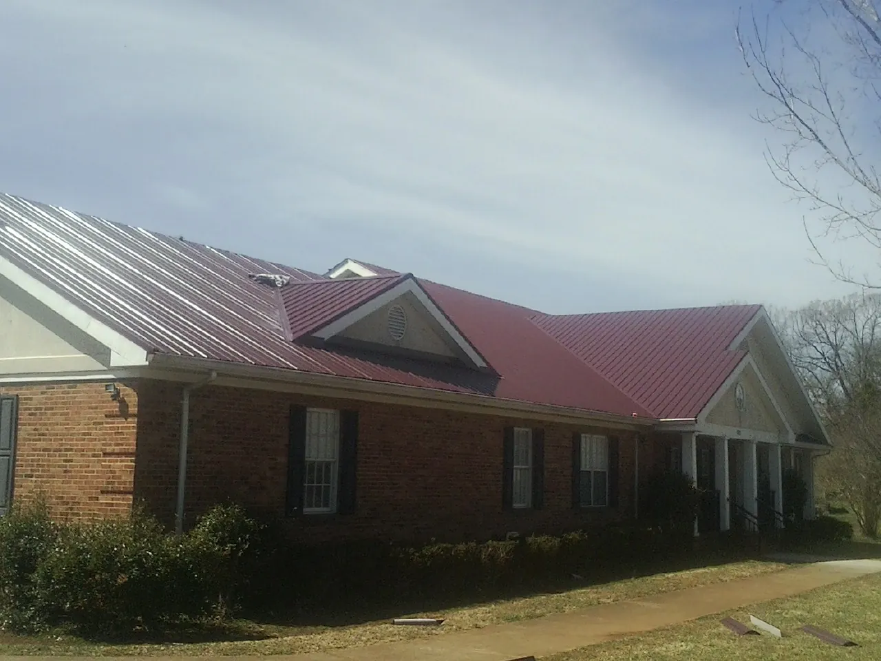 Red metal roof with gabled entries on a long brick building, from a Hail Damage Roof Repair job in Shattuck