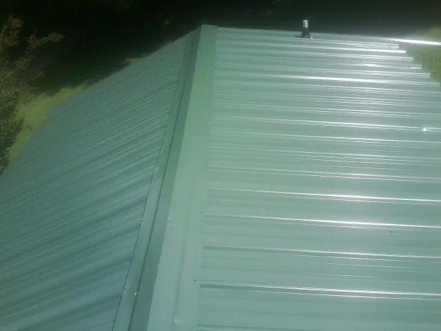 New green metal panels meeting at the ridge of a roof — Flat Roof Repair work by our crew in Shattuck