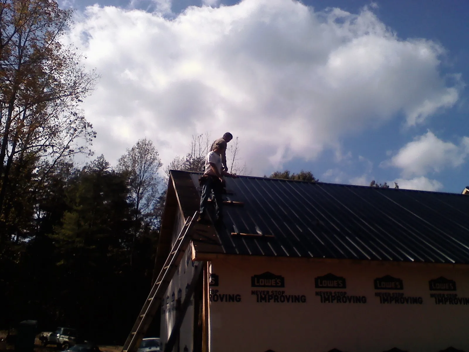 Roofer fastening dark metal panels high against a cloudy sky, from a Roof Inspection job in Shattuck
