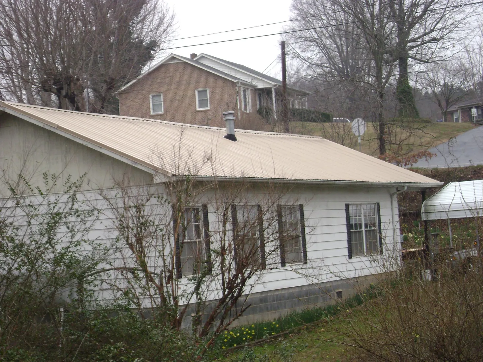 Tan metal roof on a white sided house set into a hillside — Commercial Roofing by Roofing Brothers in Shattuck