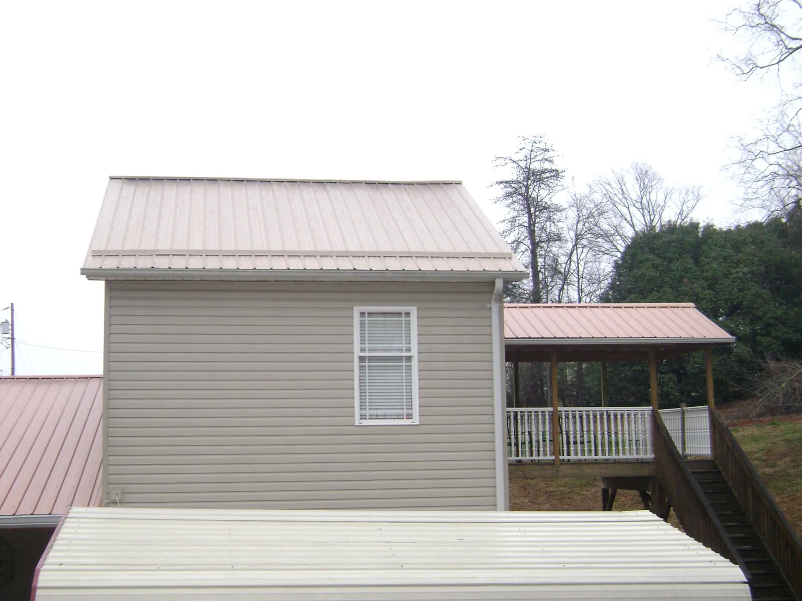 Tan metal roofs on a two story addition and attached porch, from a Roof Replacement job in Shattuck